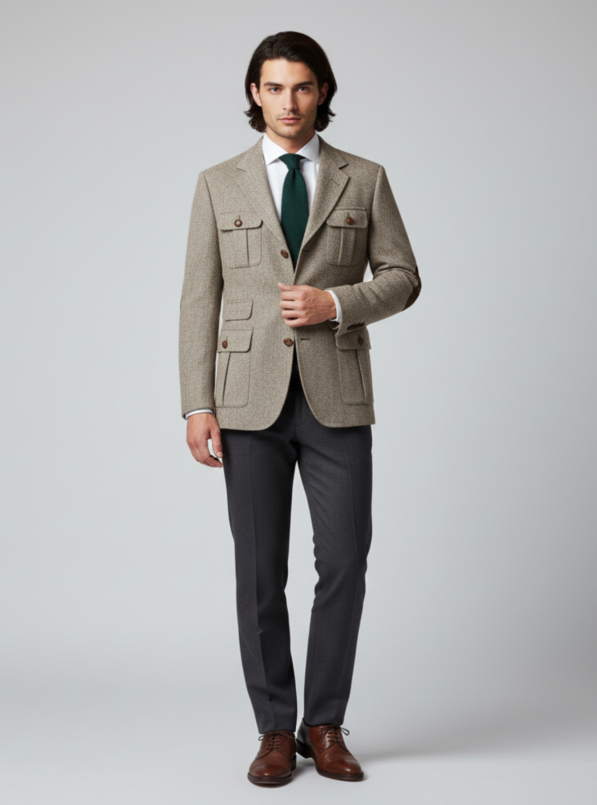 Man wearing a beige blazer, gray pants, and brown shoes on a white background