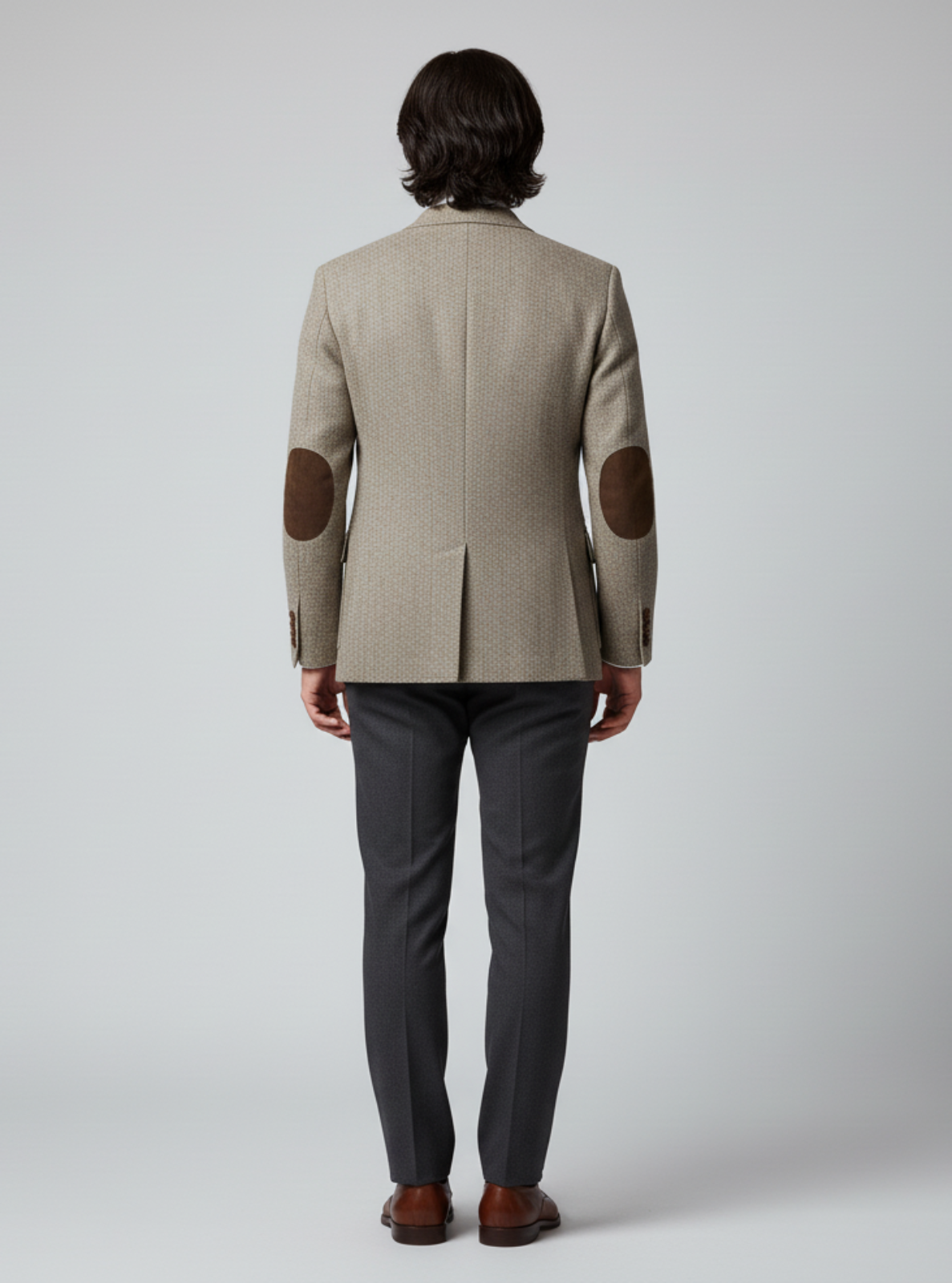 Man wearing a beige blazer with elbow patches on a gray background