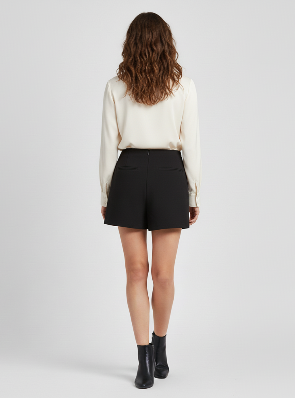 Woman wearing a white blouse and black shorts on a plain background