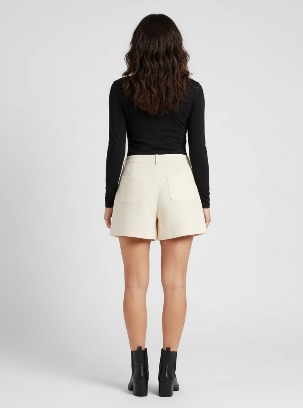 Person wearing a black long-sleeve top and cream shorts on a white background