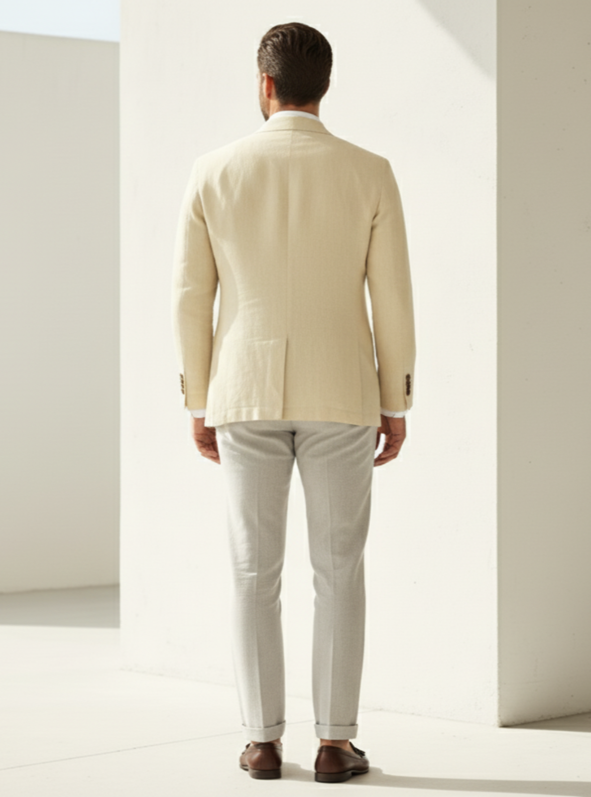 Man wearing a beige suit standing in a minimalistic room with white walls.