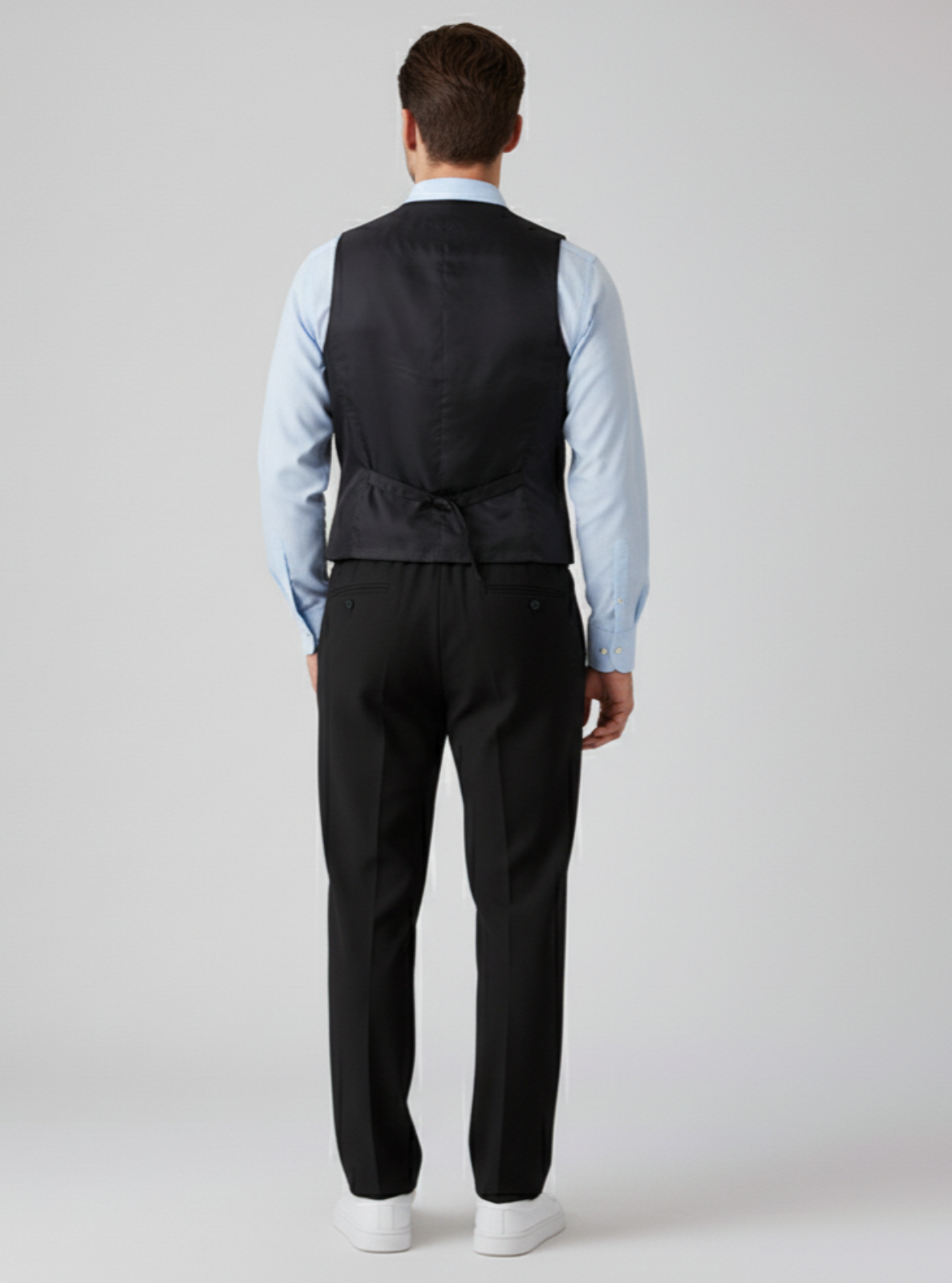 Man wearing a black vest and pants with a light blue shirt on a white background