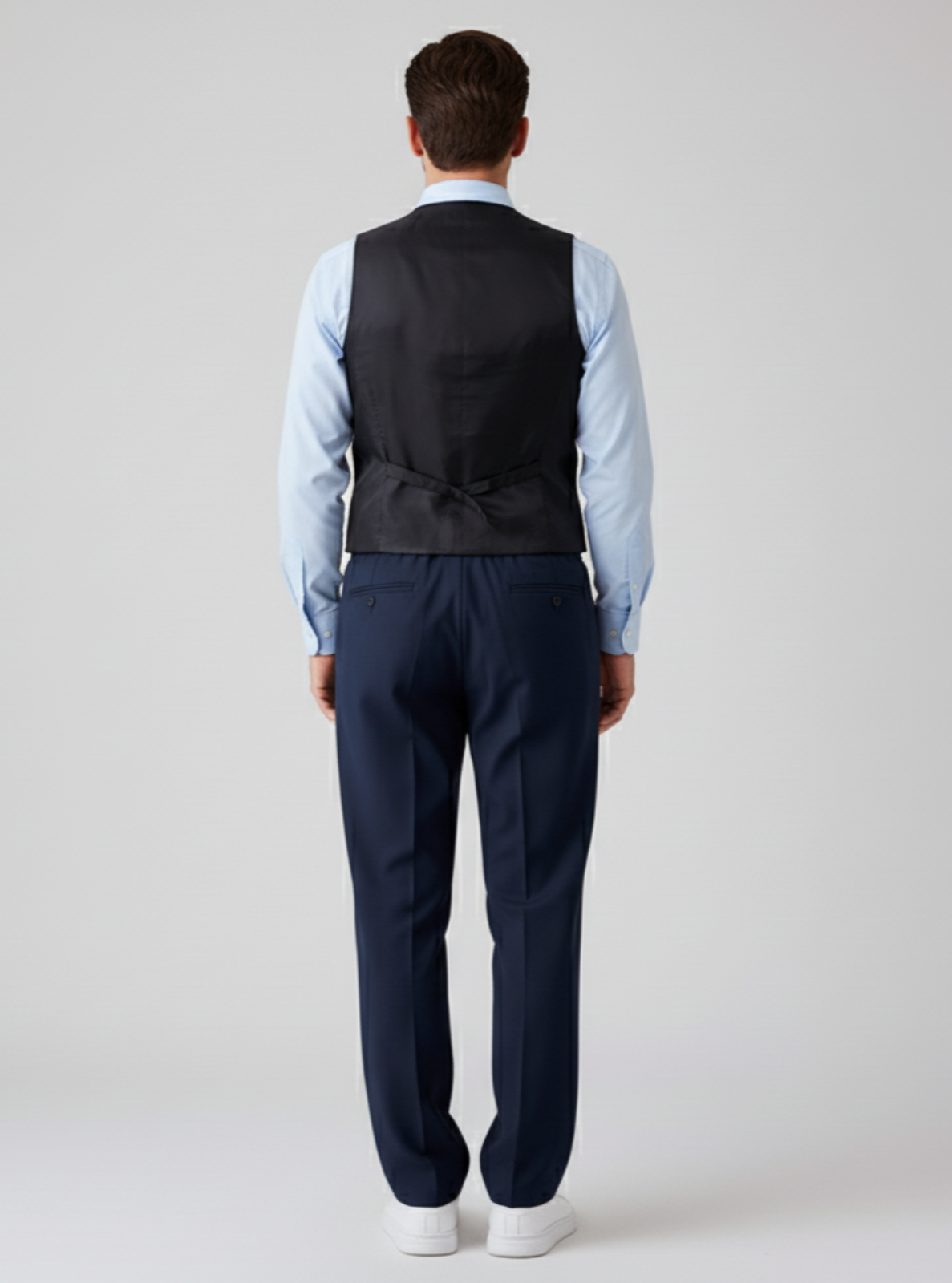 Man wearing a navy vest and pants with a light blue shirt on a white background
