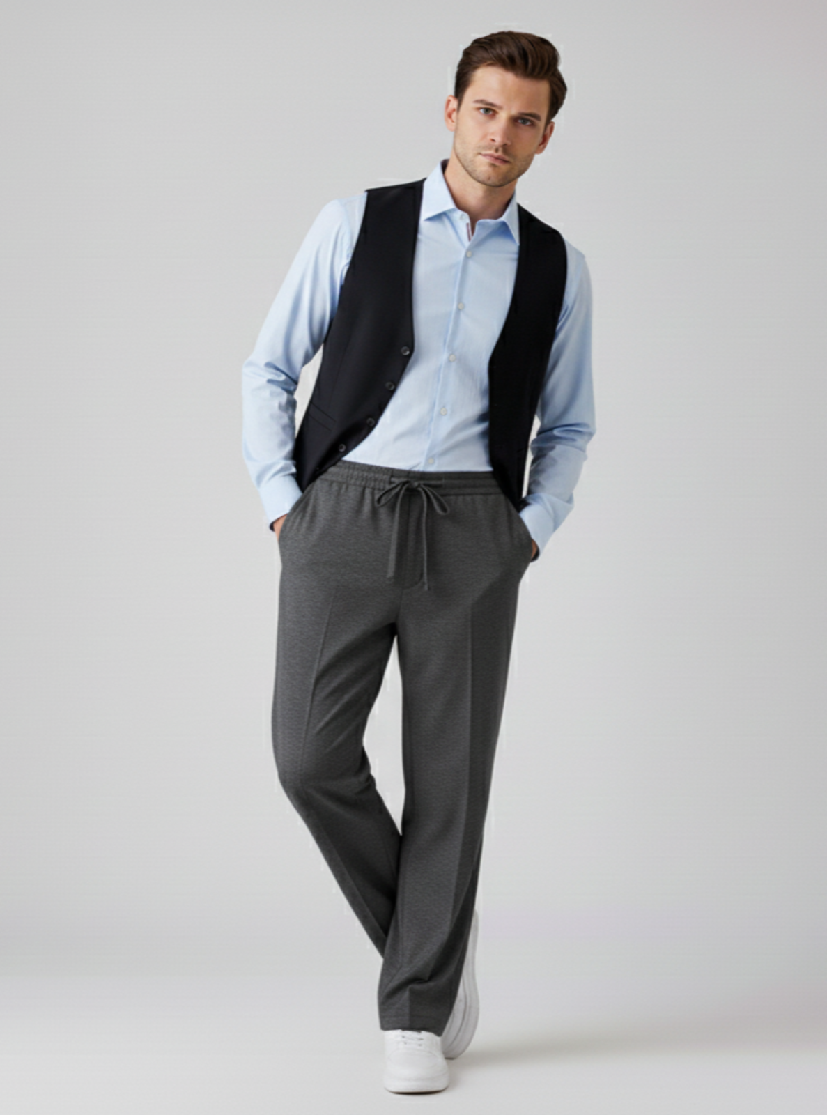 Man wearing a light blue shirt, black vest, gray pants, and white shoes on a light gray background