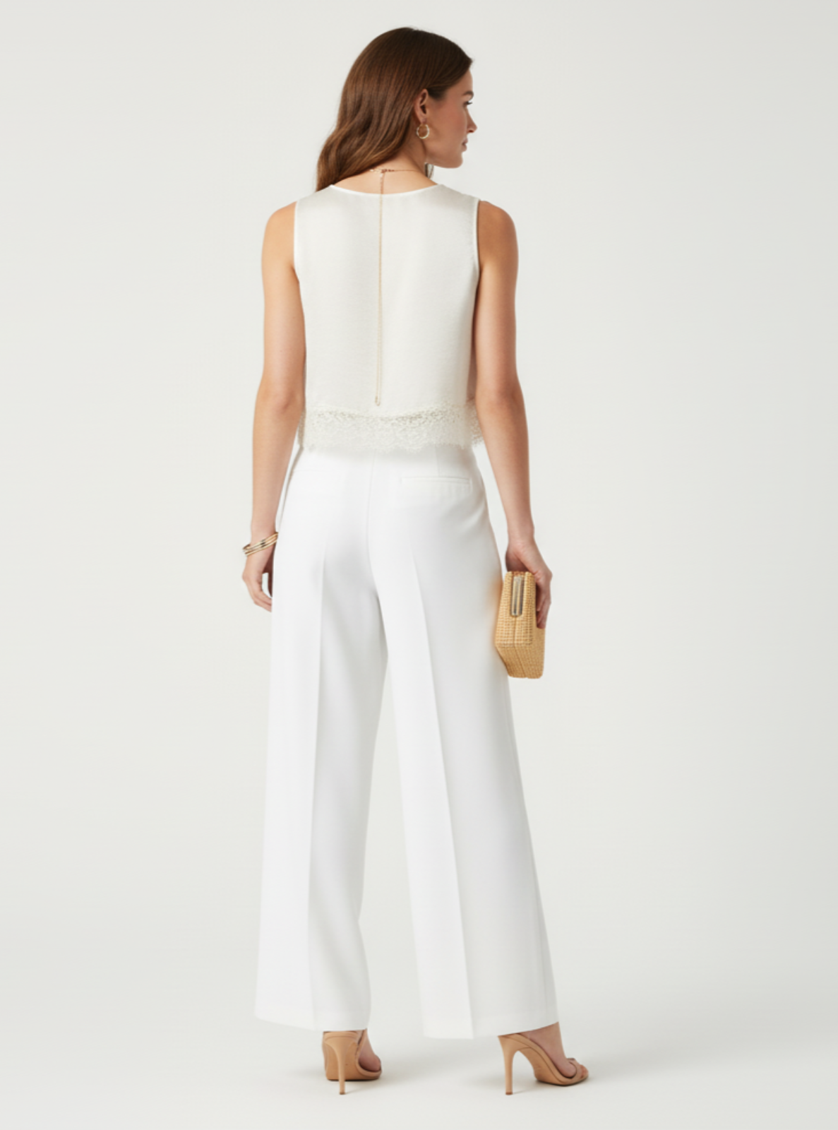 Woman wearing a white sleeveless top and pants on a plain background
