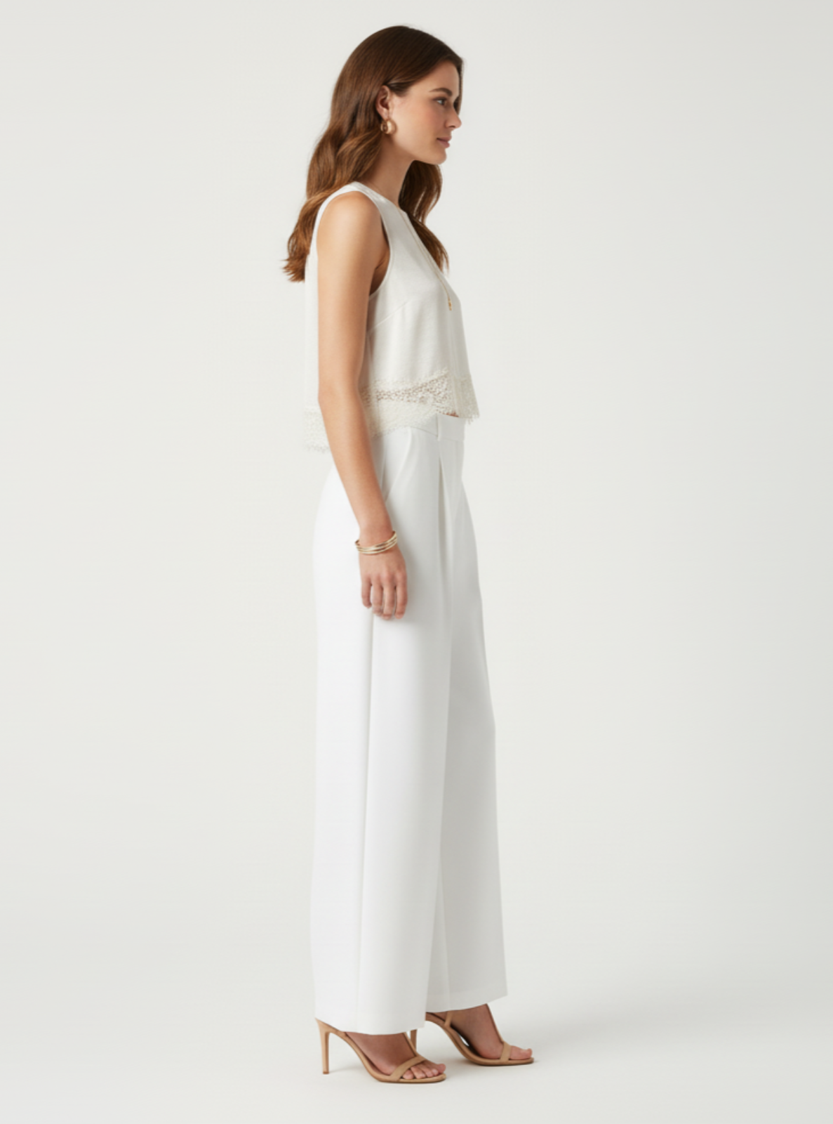 Woman wearing a white sleeveless top and high-waisted pants on a white background