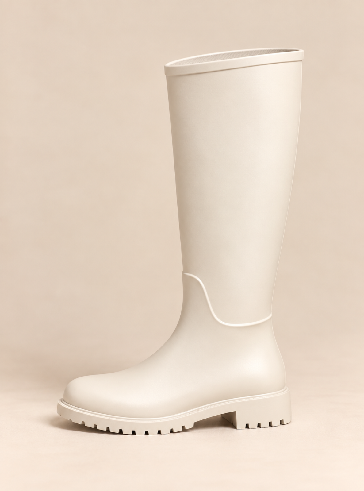 A single tall matte rain boot in a warm off-white or cream color, shown from a side profile against a solid beige background.