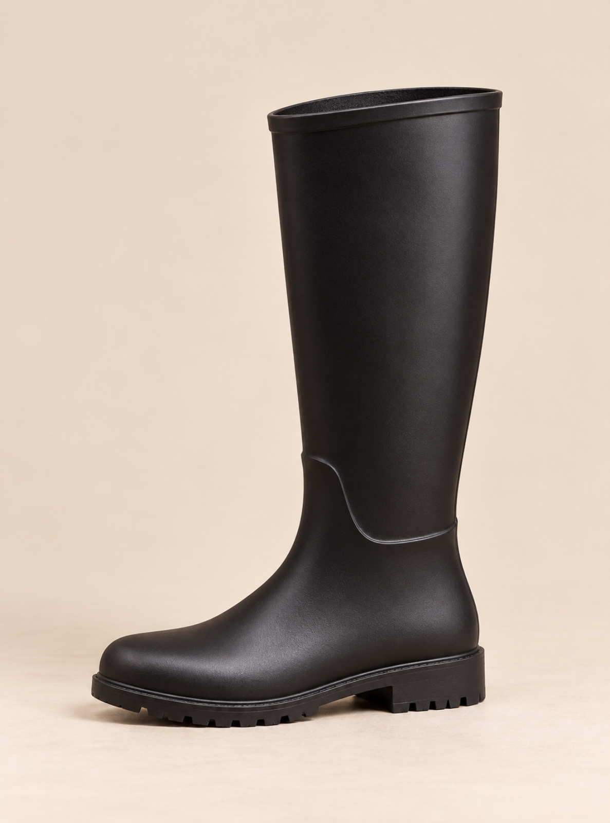 A single black knee-high rain boot with a low block heel and lug sole, shown against a solid beige background.