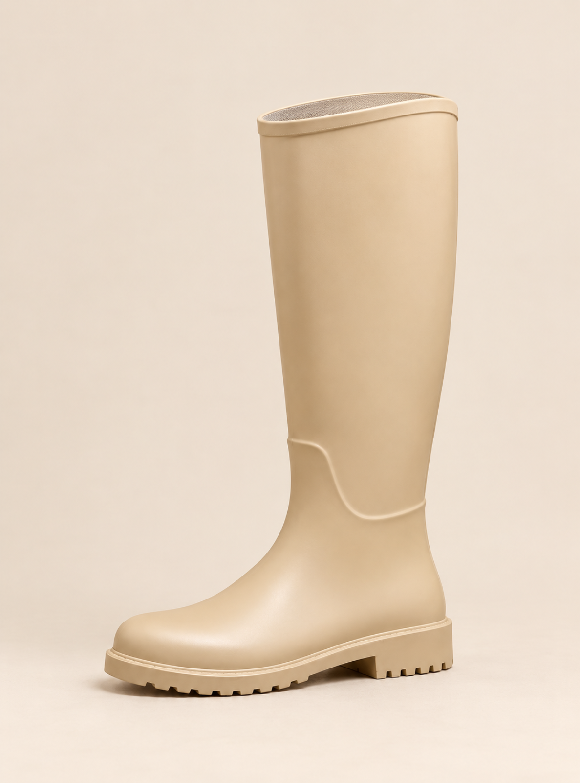 A single knee-high rubber rain boot in a light beige color, shown from a side profile against a solid, warm beige background.