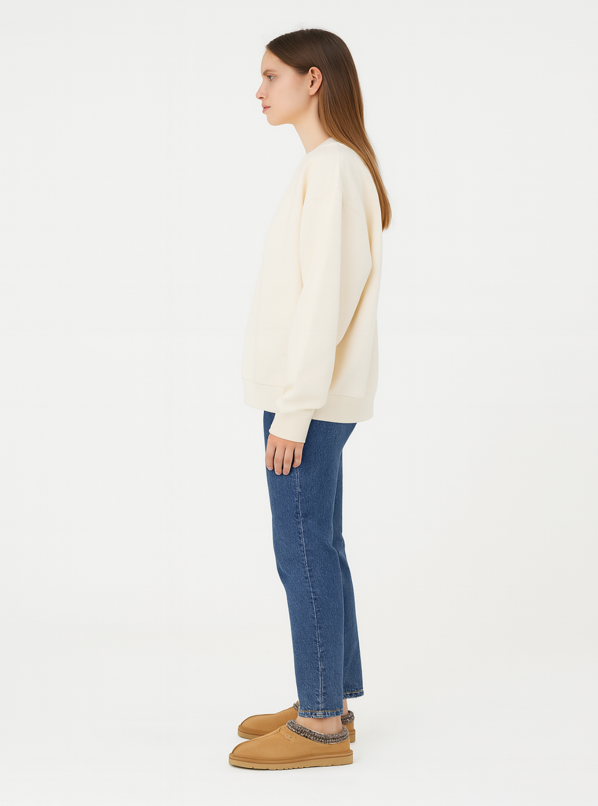 Woman wearing a cream sweater, blue jeans, and tan boots on a white background