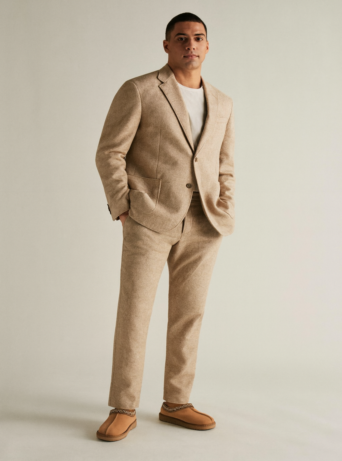 Man wearing a beige suit with a white shirt and brown shoes on a plain background