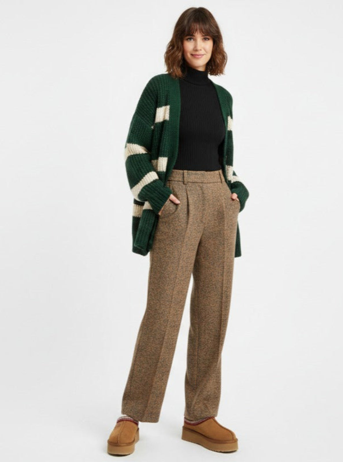 Person wearing a green and white striped cardigan, black top, brown plaid pants, and brown shoes on a white background