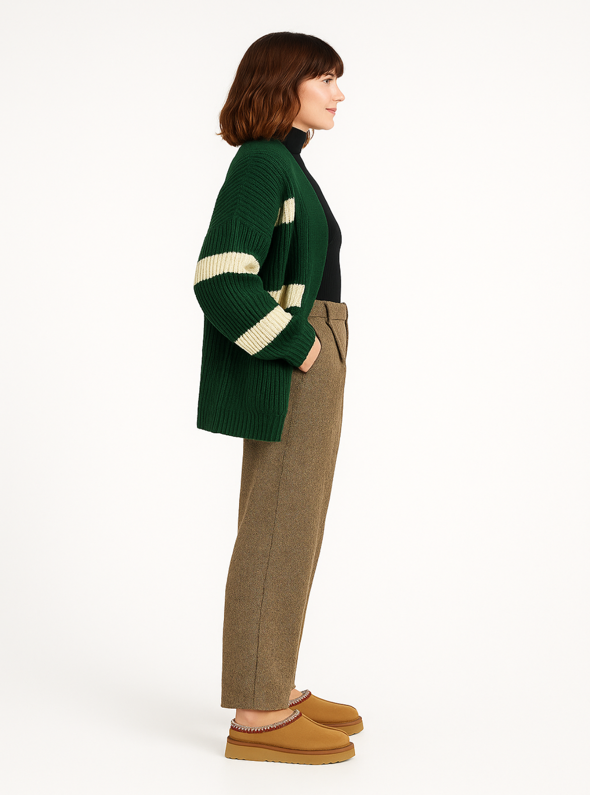 Woman wearing a green cardigan with white stripes, black top, brown pants, and tan shoes on a white background