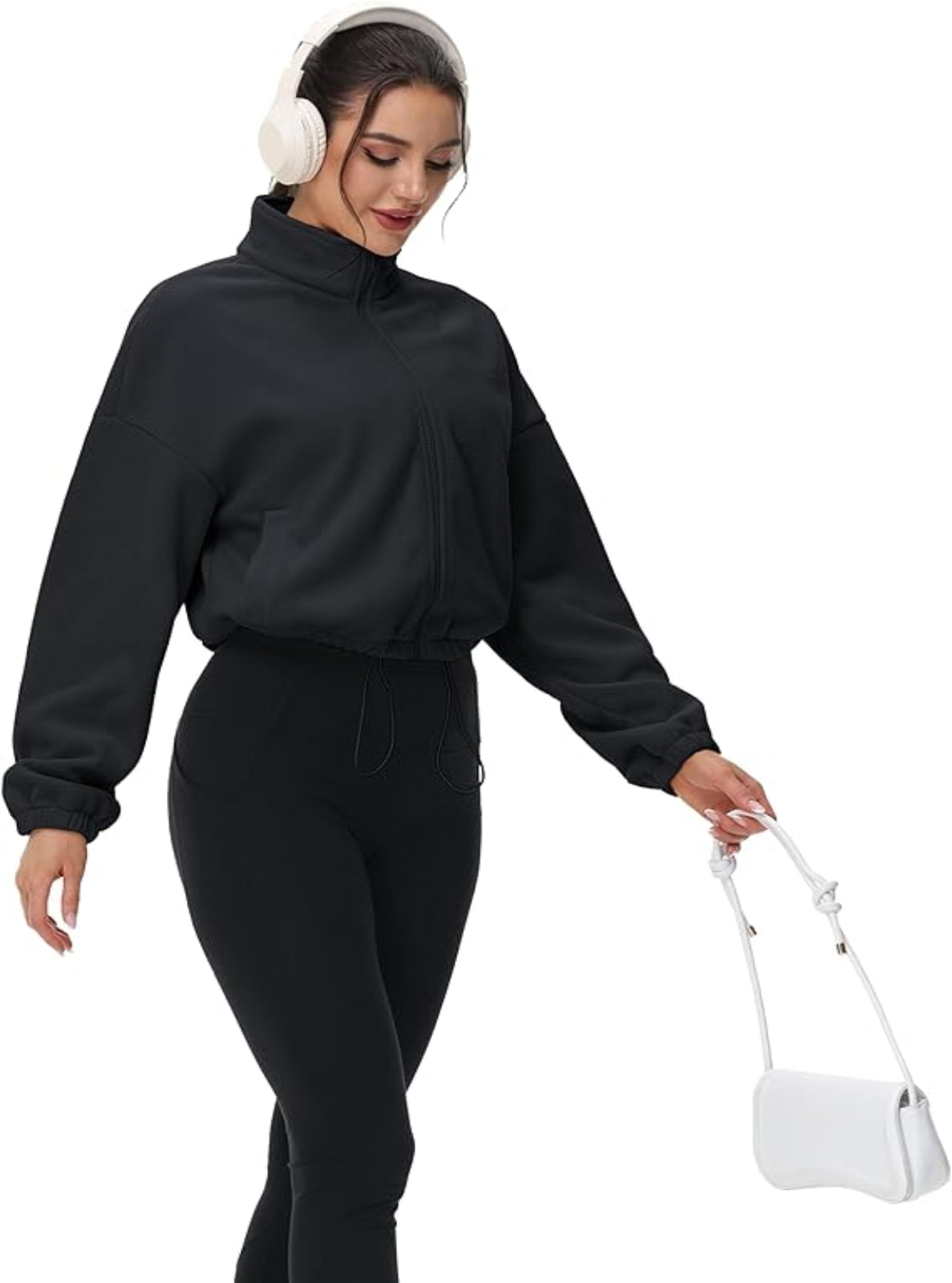 Woman wearing a black outfit with white headphones and a white handbag on a white background
