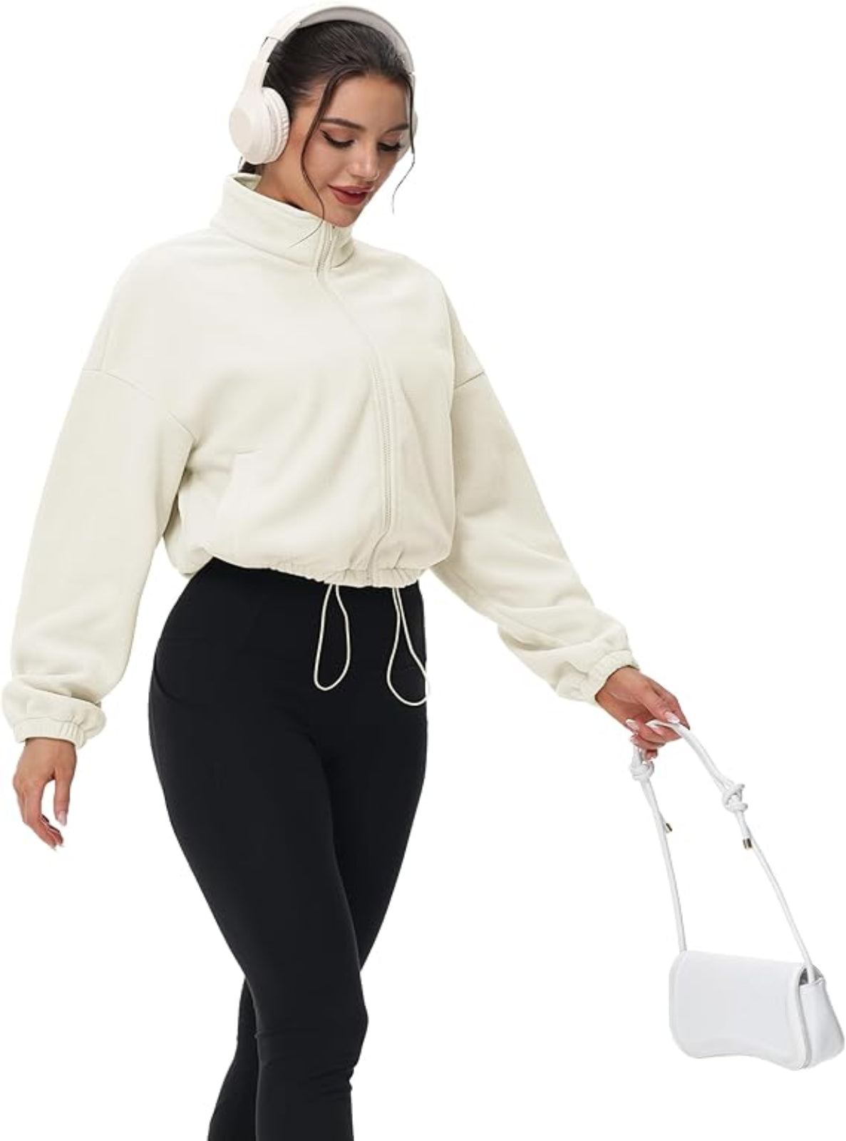 Woman wearing a cream sweater and black leggings, holding a white bag on a white background