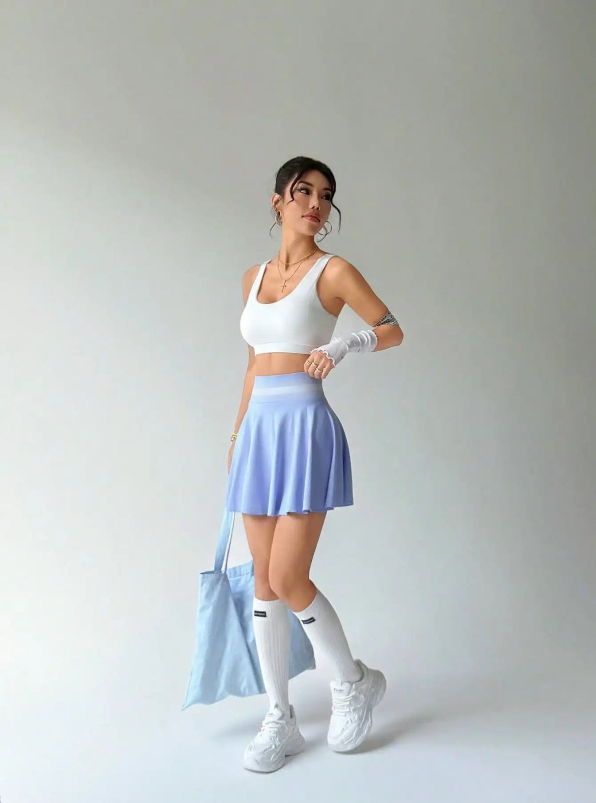 Woman in athletic wear with a light blue bag against a plain background