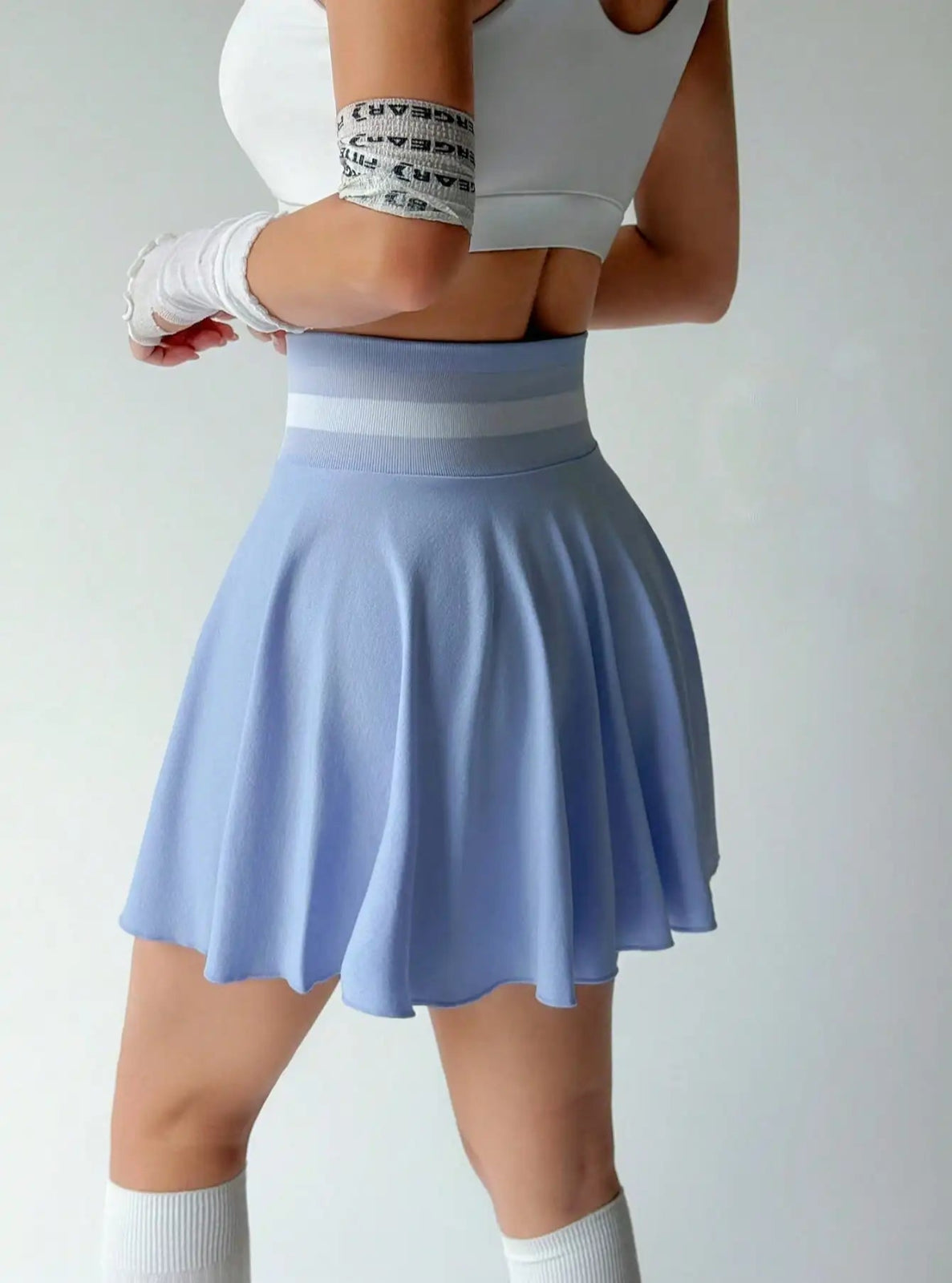 Person wearing a light blue skirt with a white top on a plain background