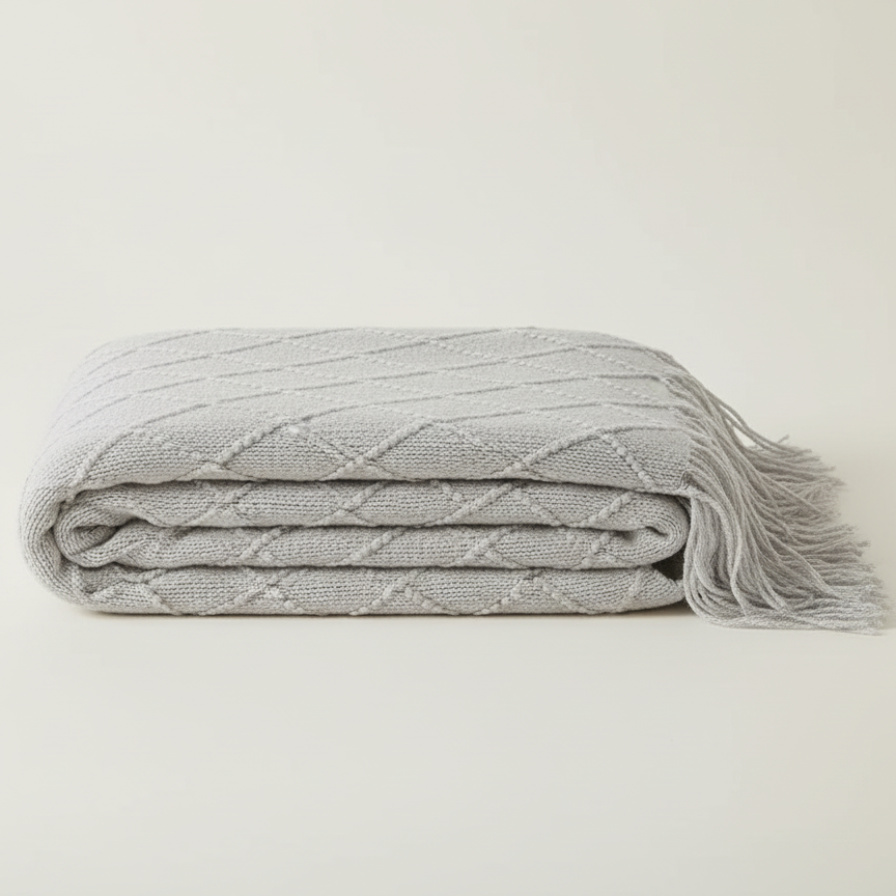 Folded gray blanket with tassels on a light beige background