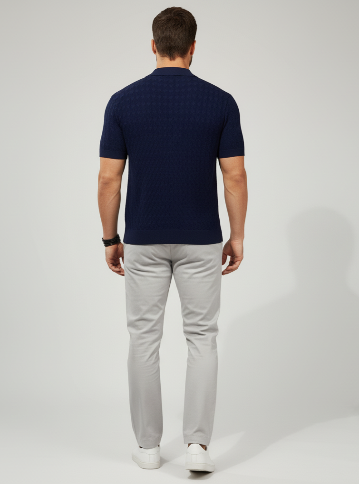 Man wearing a navy polo shirt and light gray pants on a white background