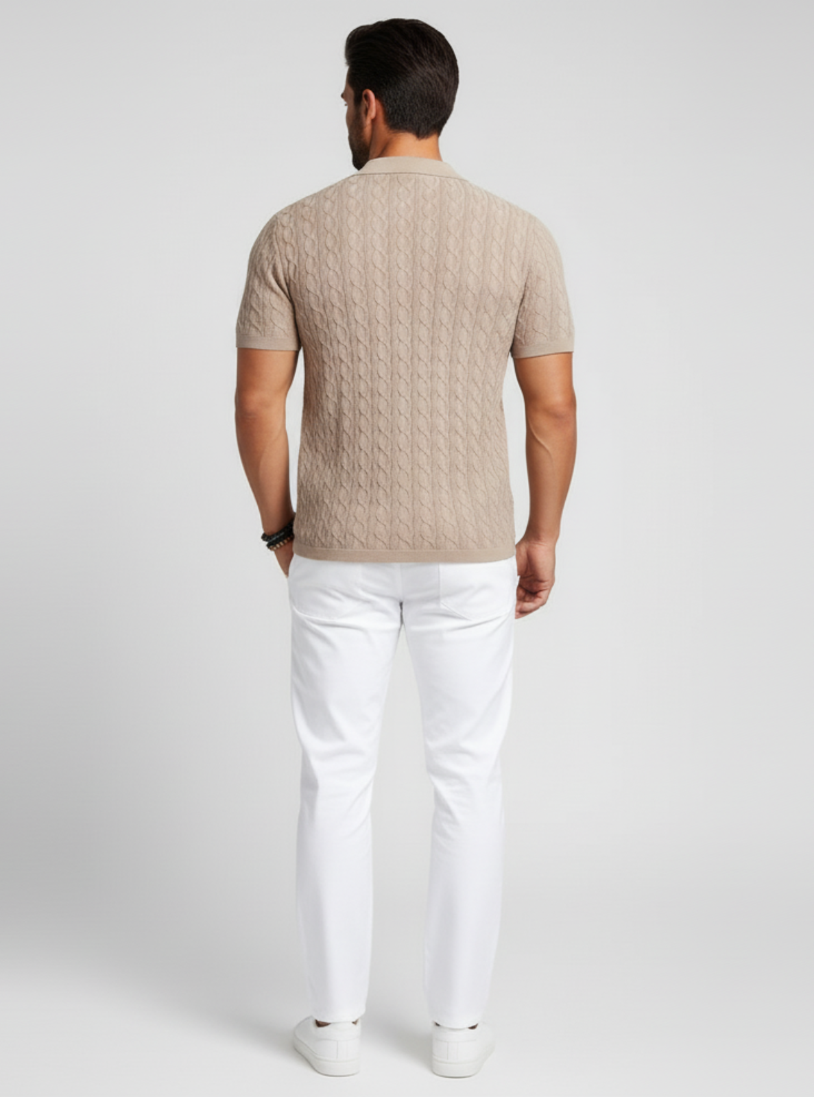 Man wearing a beige knitted sweater and white pants on a light gray background
