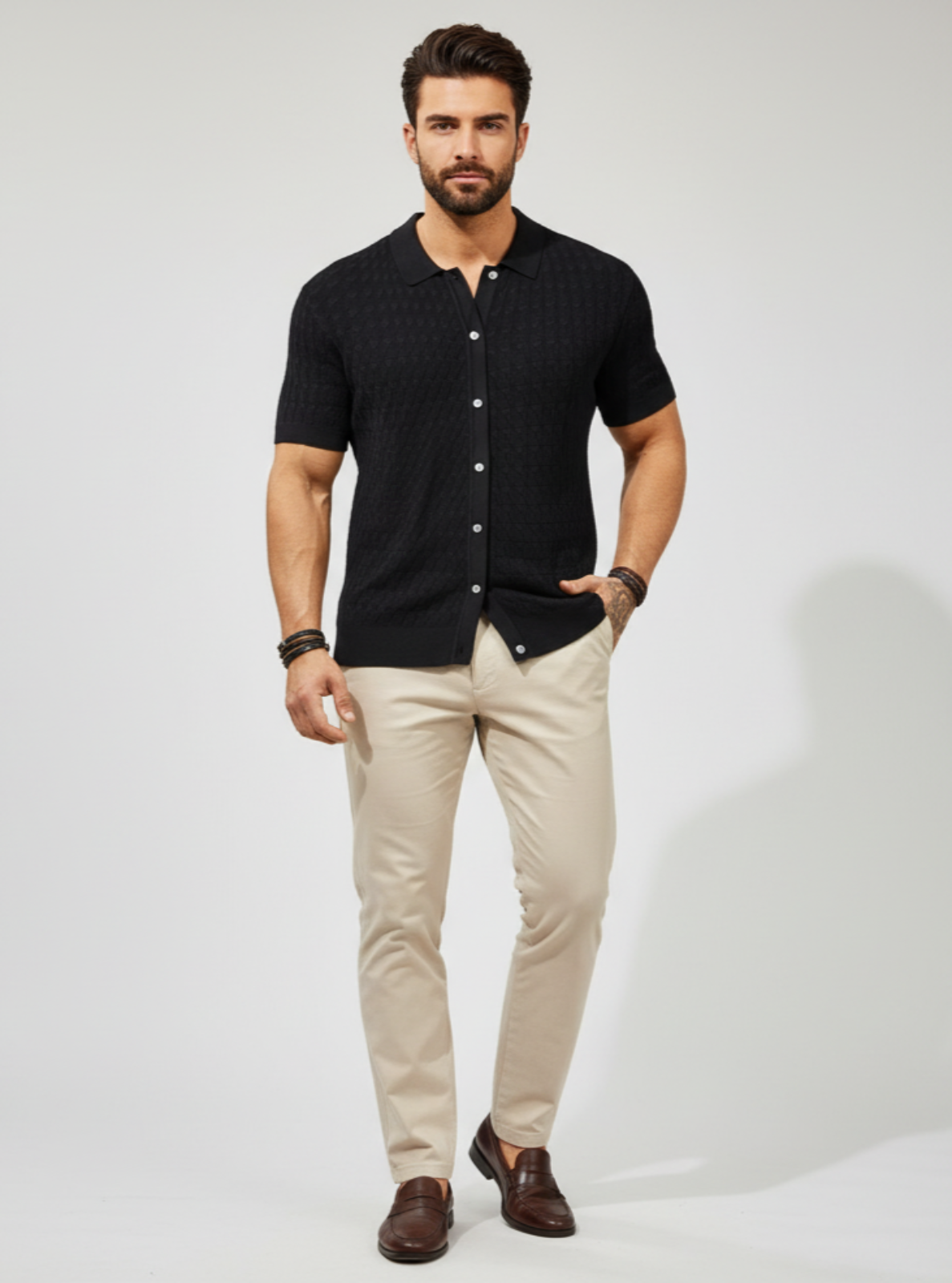 Man wearing a black short-sleeve button-up shirt, beige pants, and brown shoes on a white background