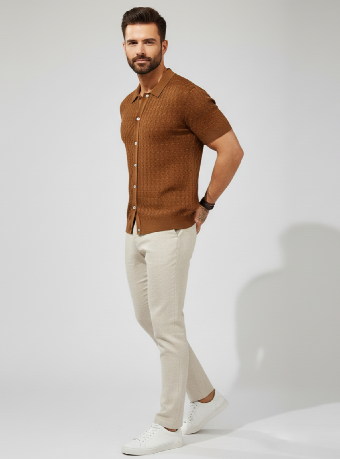 Man wearing a brown shirt and white pants on a plain background