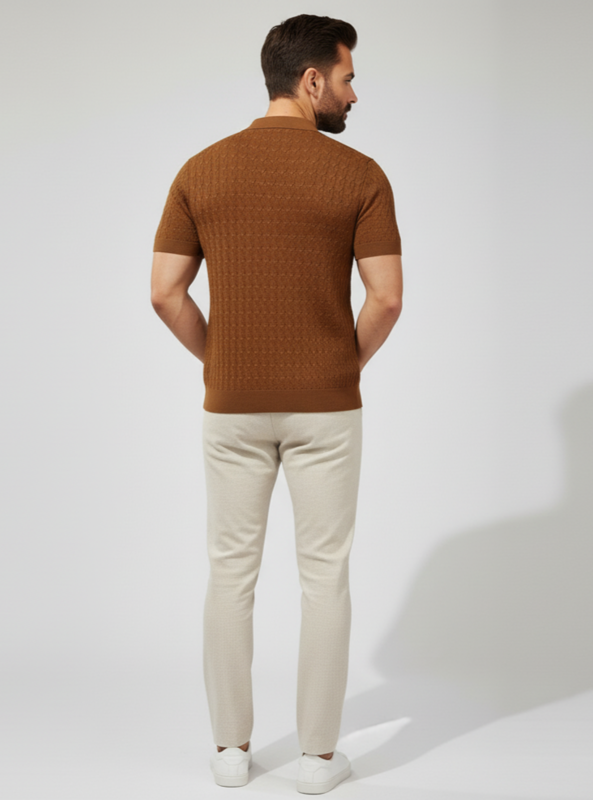 Man wearing a brown knitted sweater and beige pants on a white background