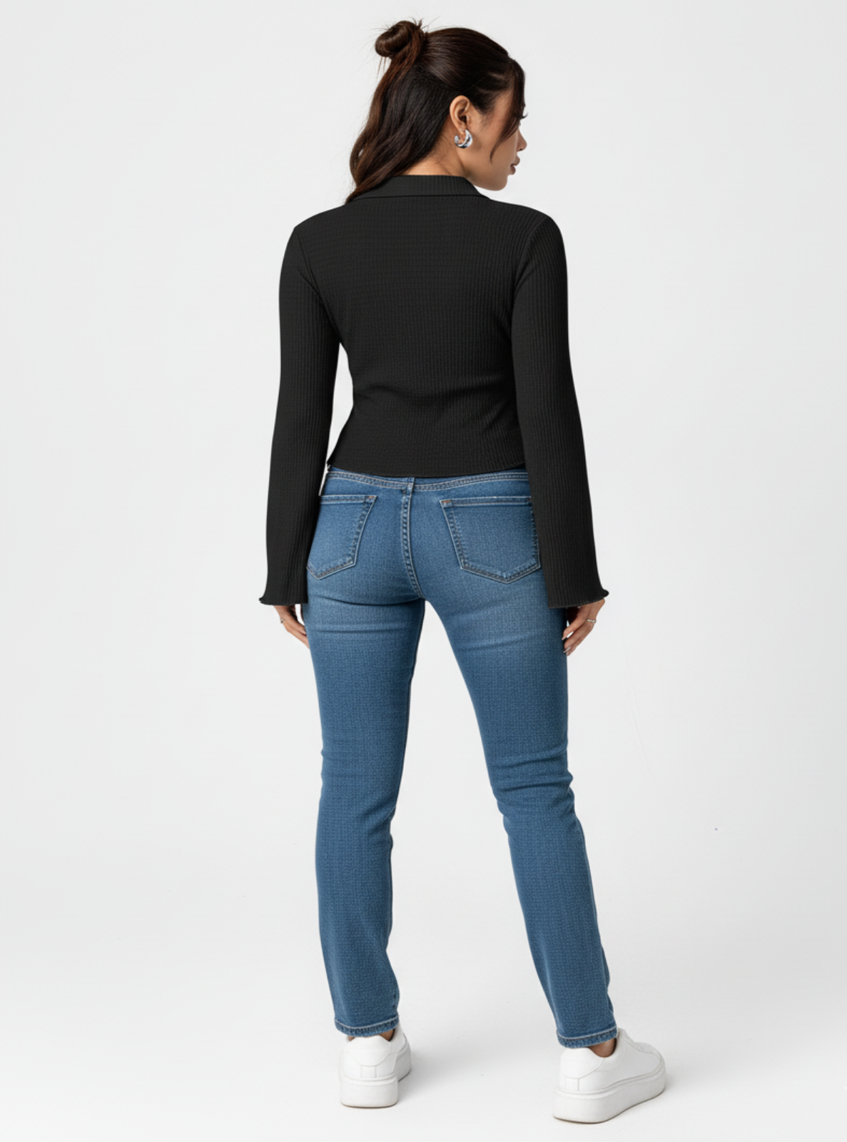 Woman wearing a black long-sleeve top and blue jeans on a white background
