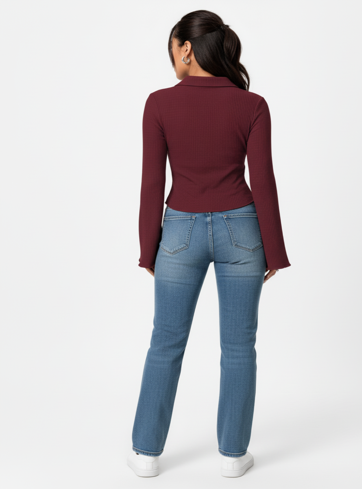 Person wearing a burgundy long-sleeve top and blue jeans on a white background