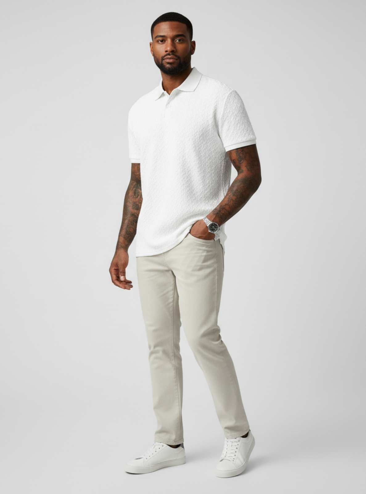 Man wearing a white polo shirt and light gray pants on a plain background