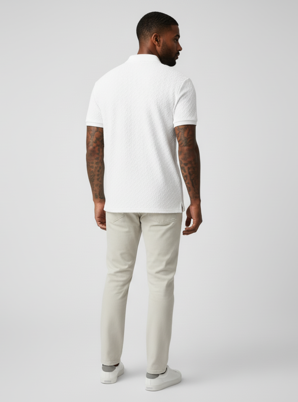 Man wearing a white polo shirt and light gray pants on a plain background