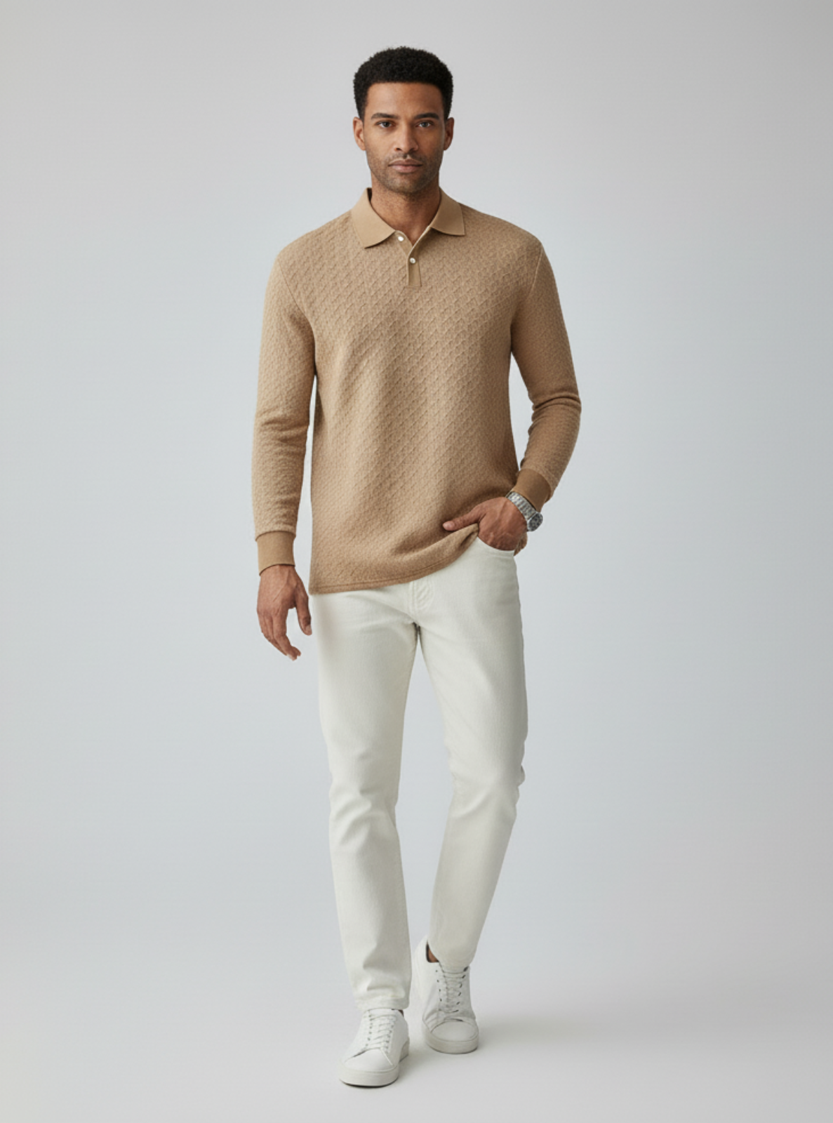 Man wearing a beige sweater and white pants on a gray background