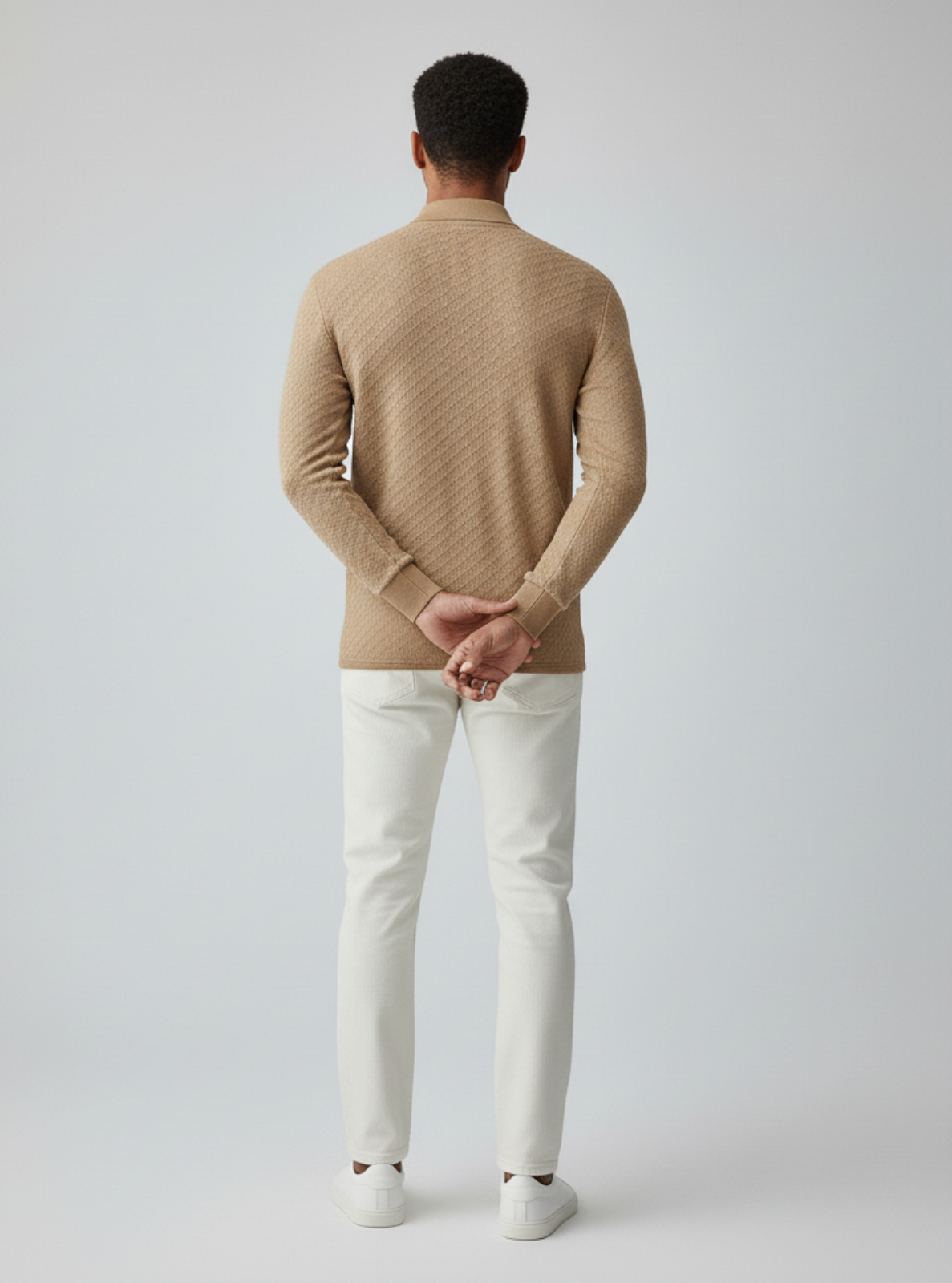 Man wearing a beige sweater and white pants on a plain background