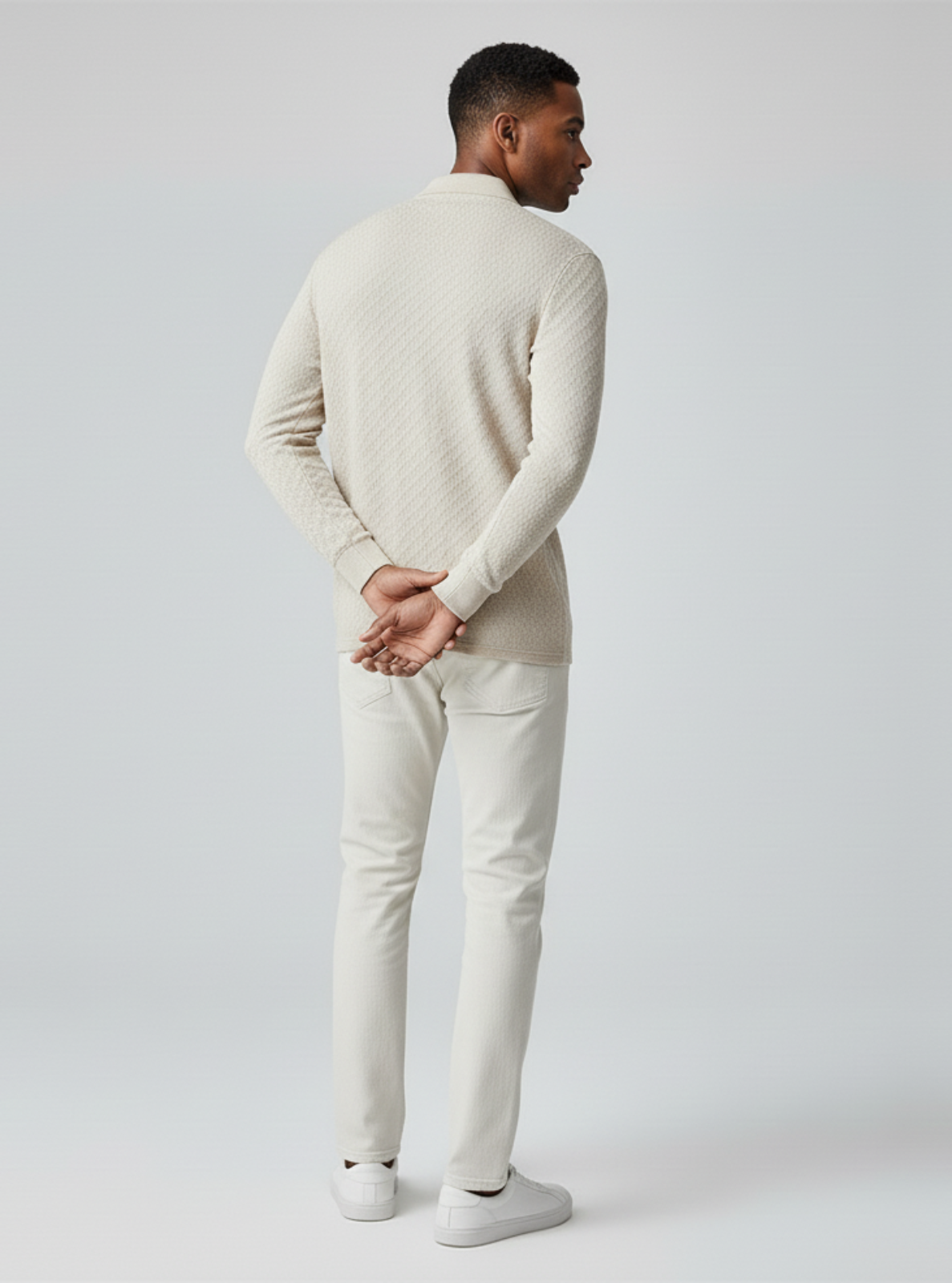 Man wearing a beige sweater and white pants on a plain background