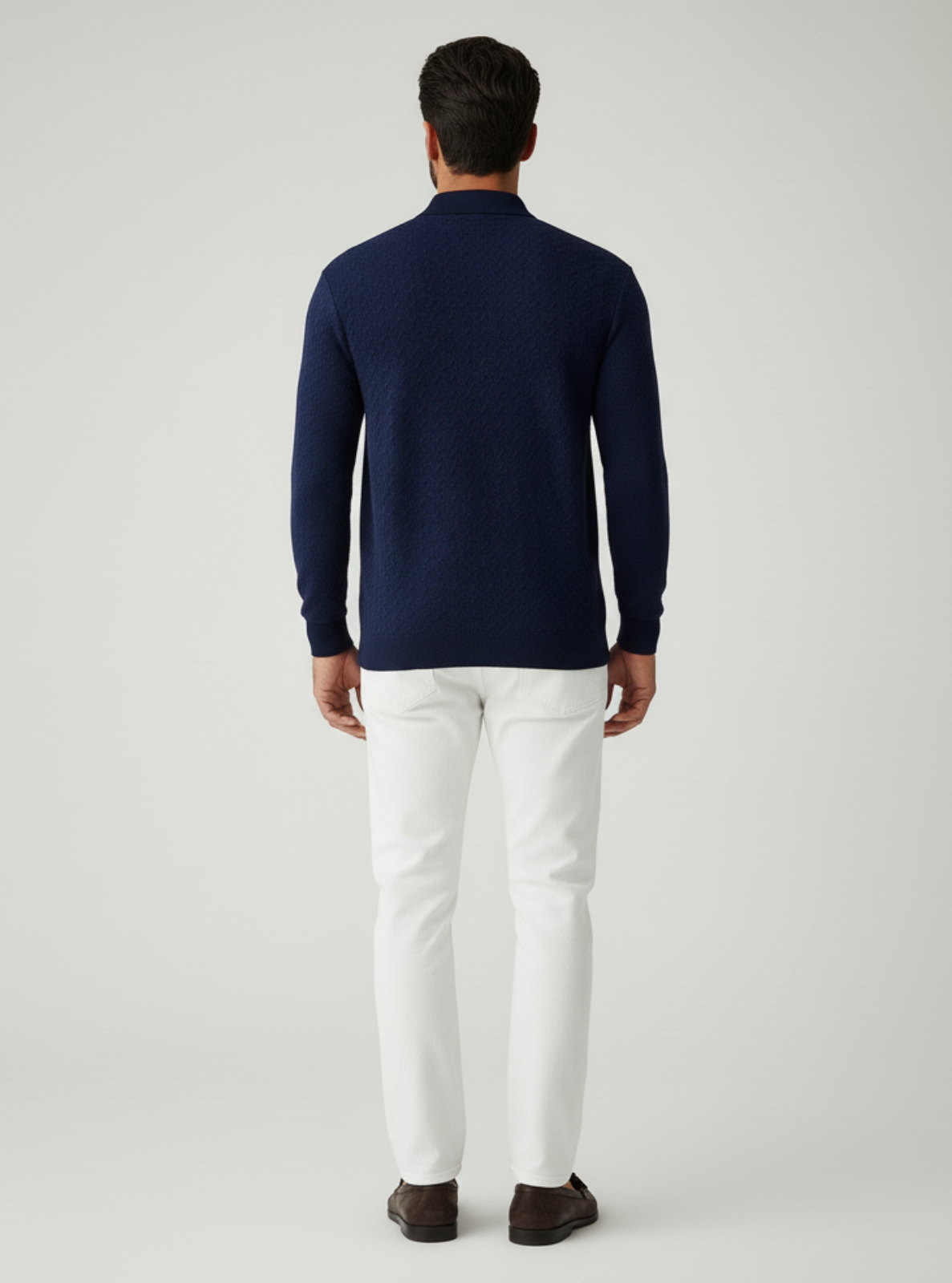 Man wearing a navy sweater and white pants on a light gray background