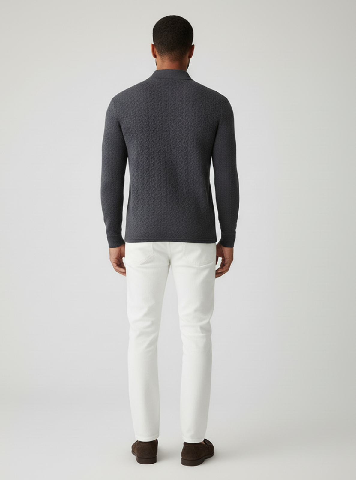 Man wearing a dark gray patterned sweater and white pants on a light gray background