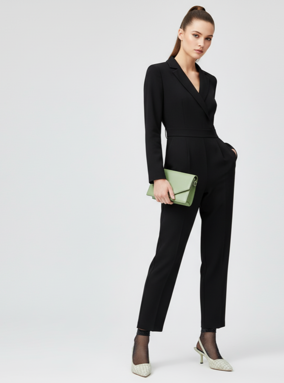 Woman in a black suit holding a green clutch against a white background