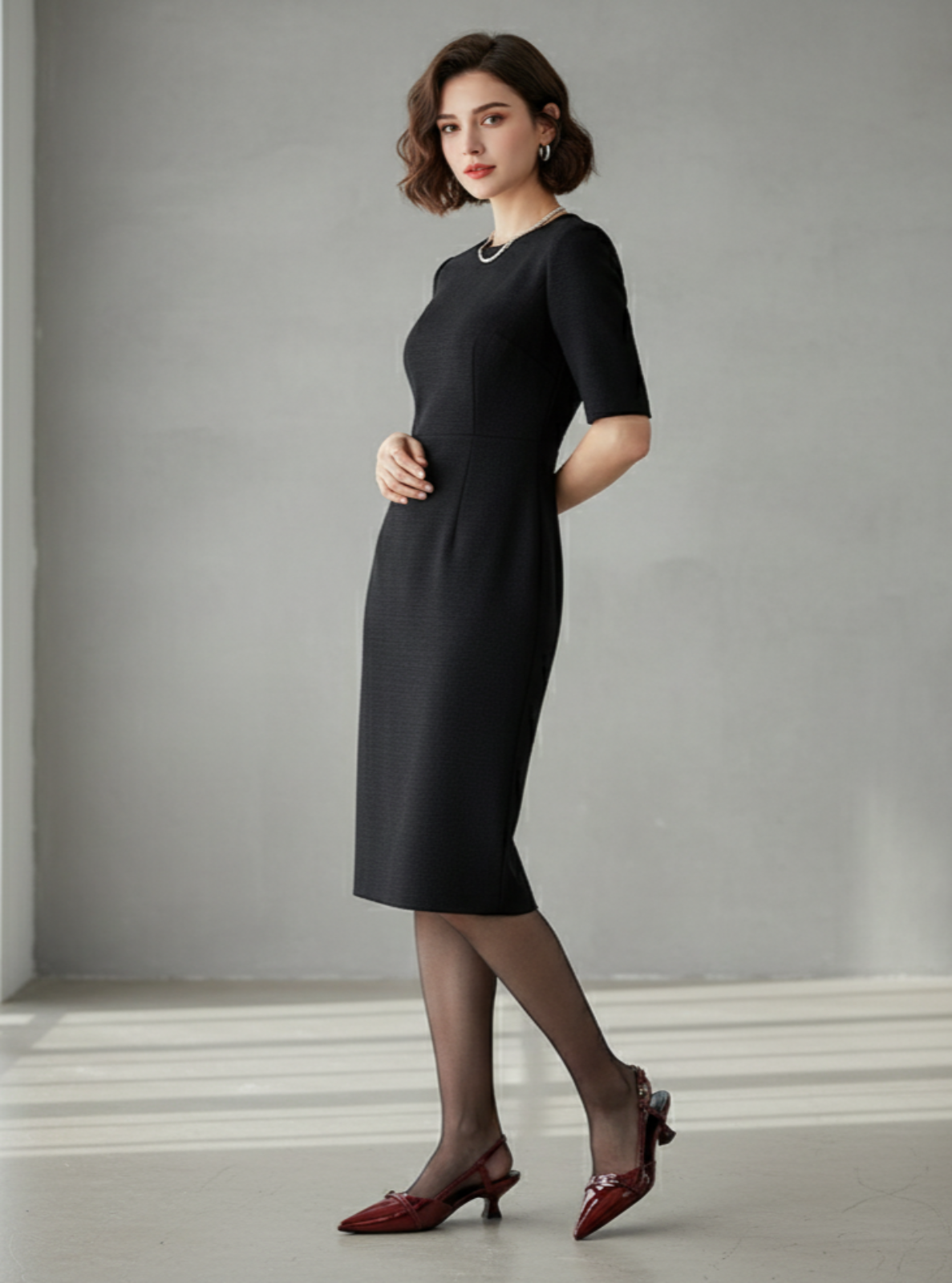 Woman wearing a black dress standing in a minimalistic room with light gray walls and white floor.