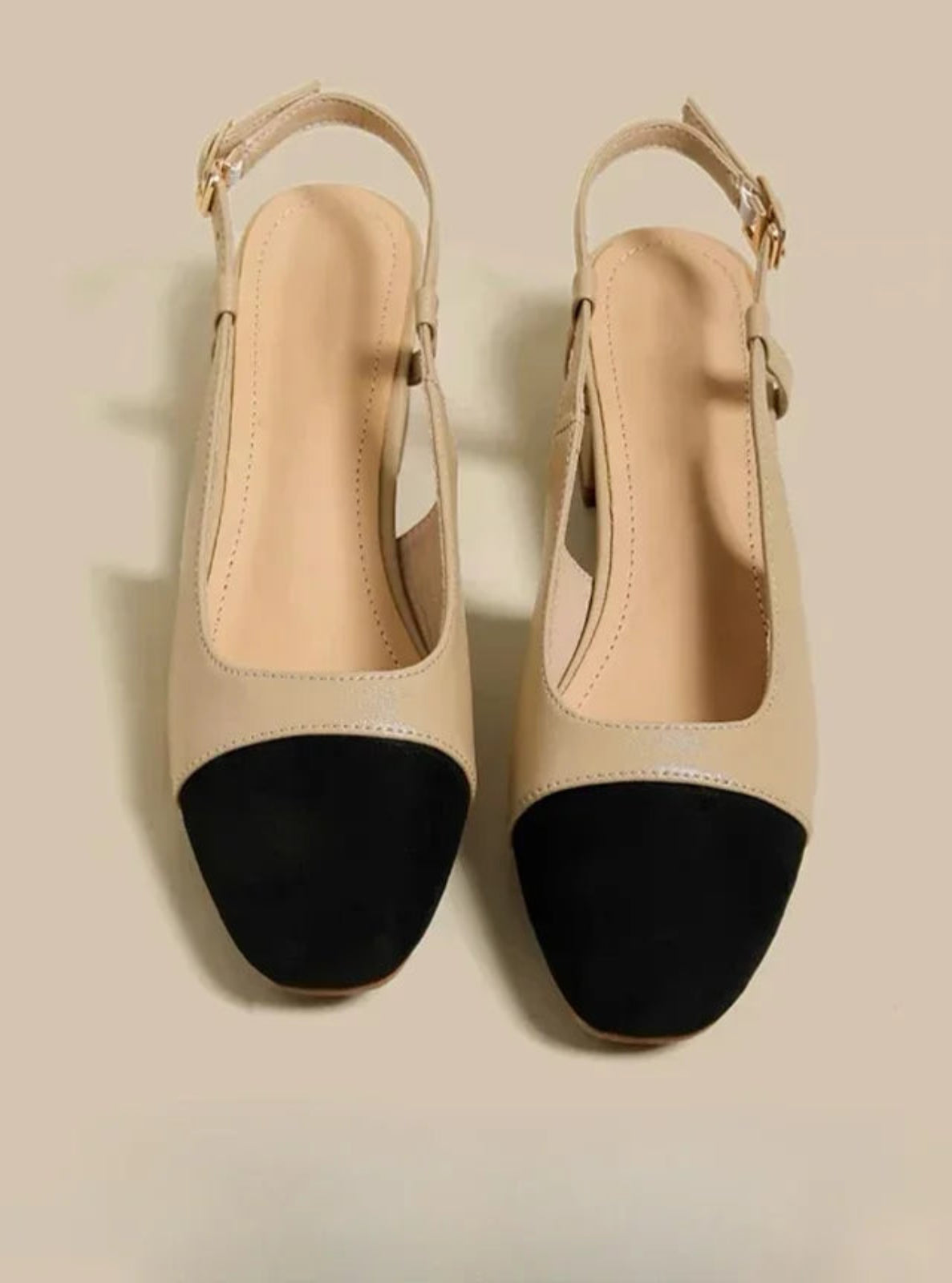 Pair of beige high heels with black soles on a beige background
