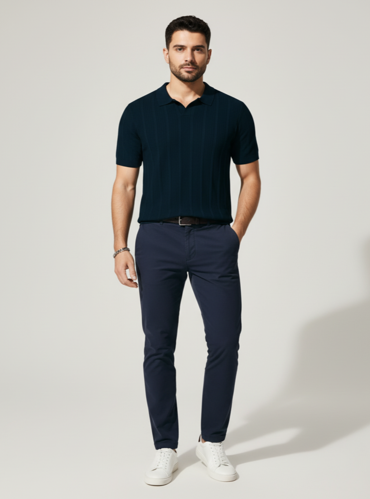 Man wearing a navy polo shirt and pants with white shoes on a light gray background