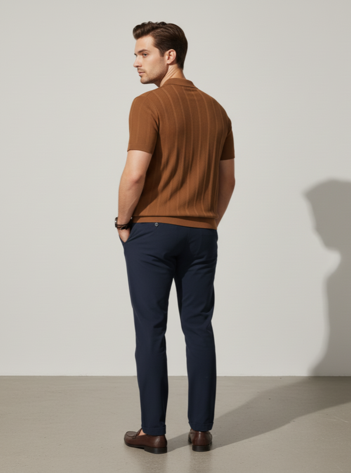 Man wearing a brown polo shirt and navy pants against a plain background