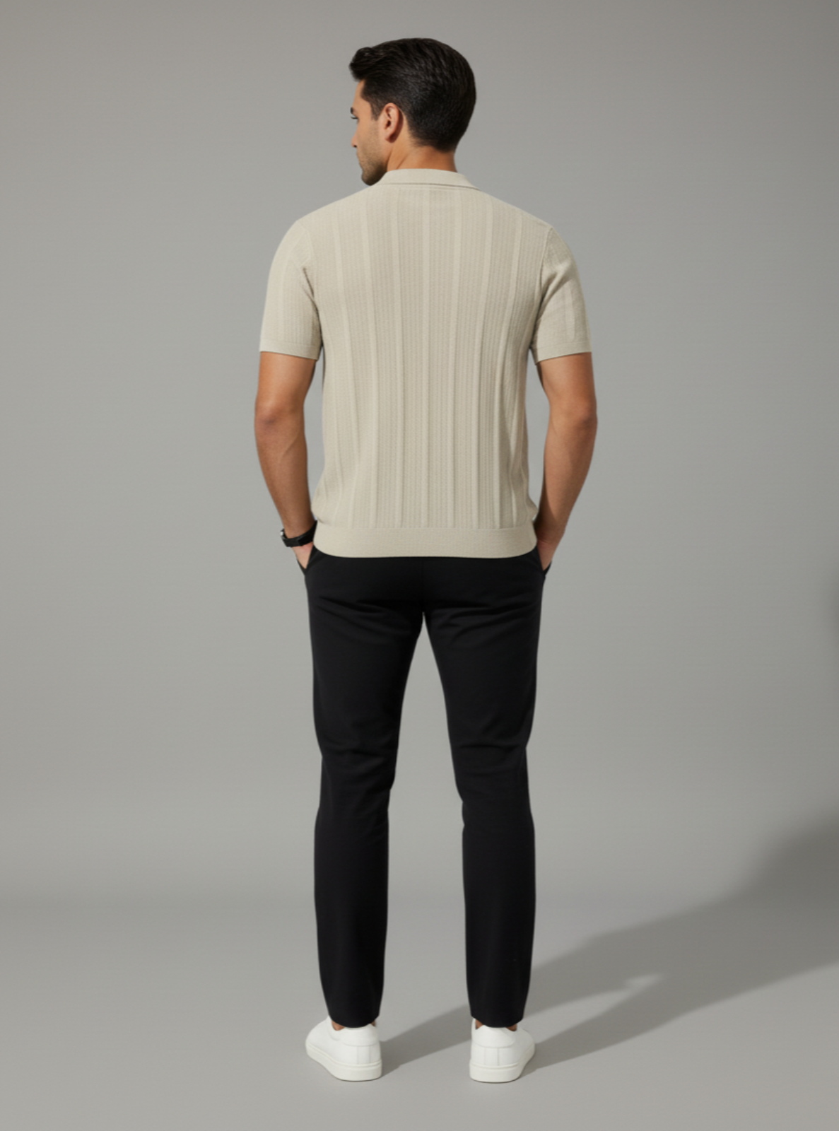 Man wearing a beige ribbed sweater and black pants on a gray background