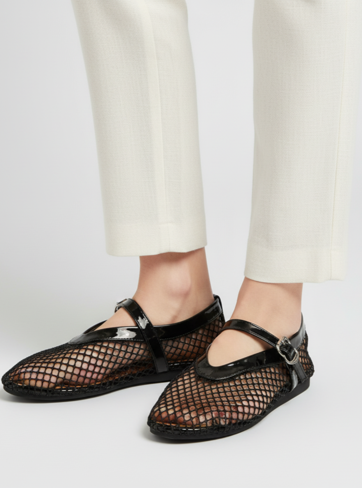 Black mesh sandals worn with white pants on a light gray background