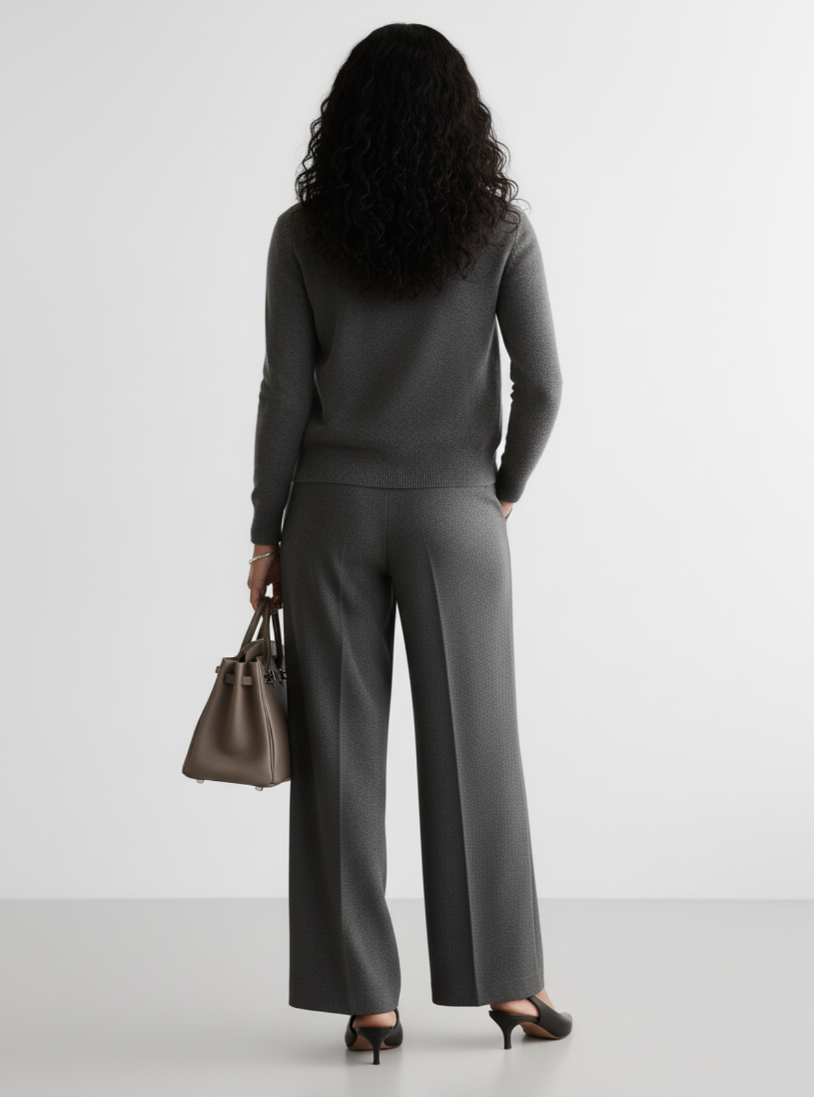 Woman wearing a gray suit holding a brown handbag on a white background