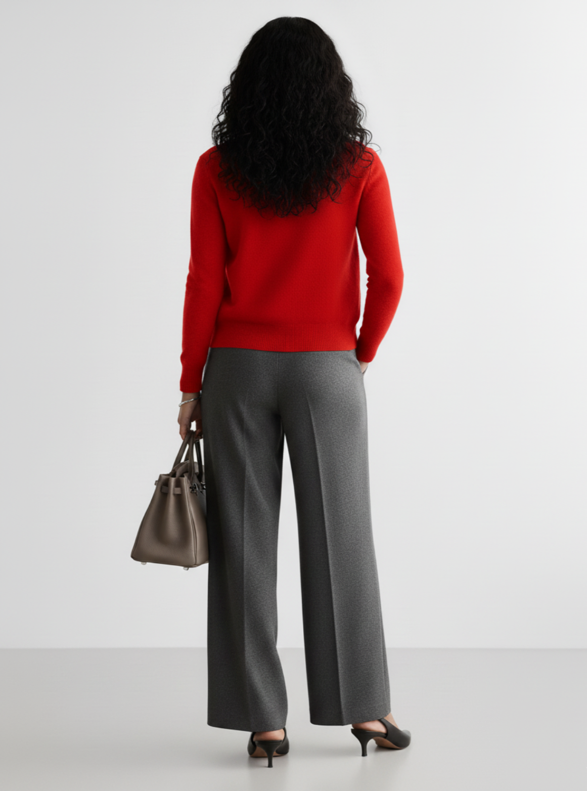 Woman wearing a red sweater and gray pants with a handbag on a white background