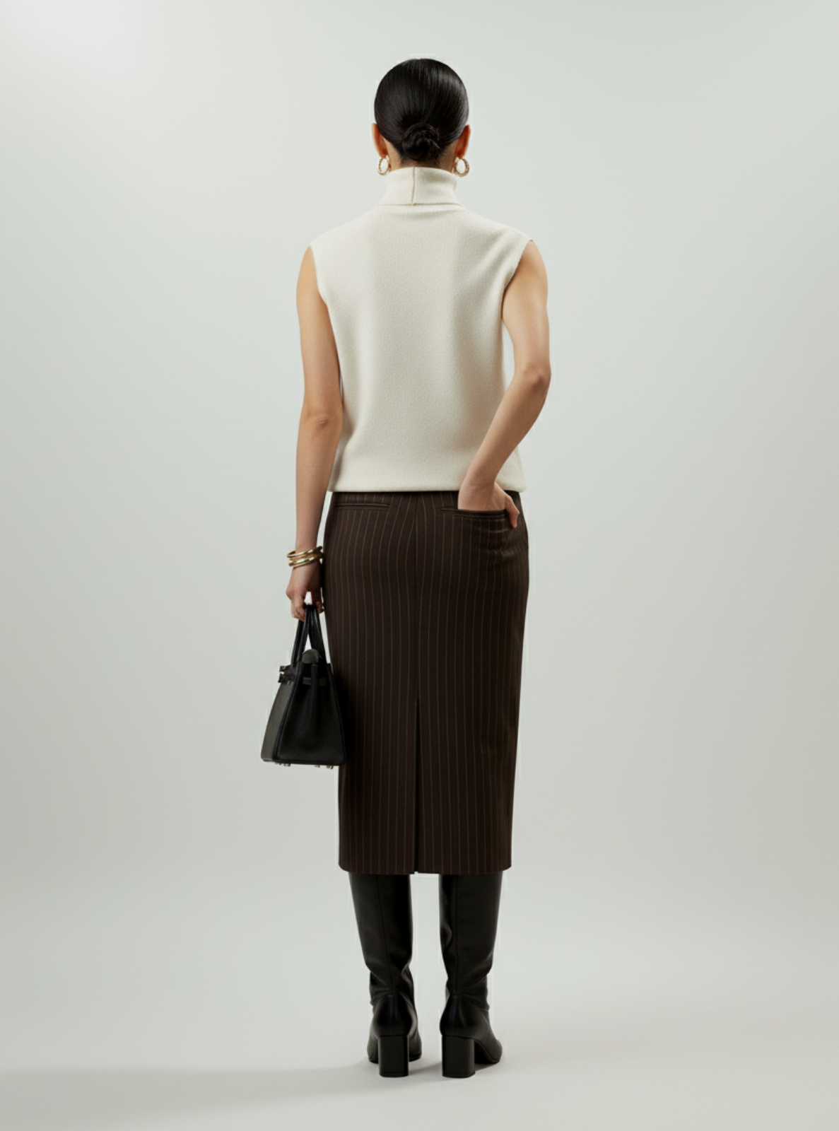 Person wearing a white sleeveless top and brown skirt with a black handbag on a light gray background