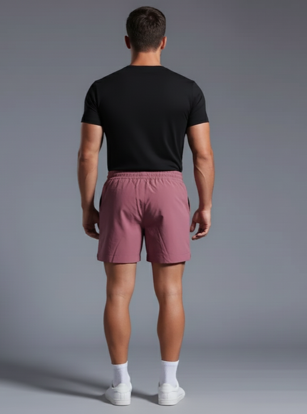 Man wearing a black t-shirt and pink shorts on a gray background