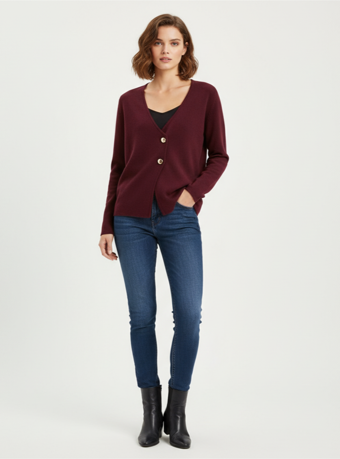 Woman wearing a burgundy cardigan, black top, blue jeans, and black boots on a white background
