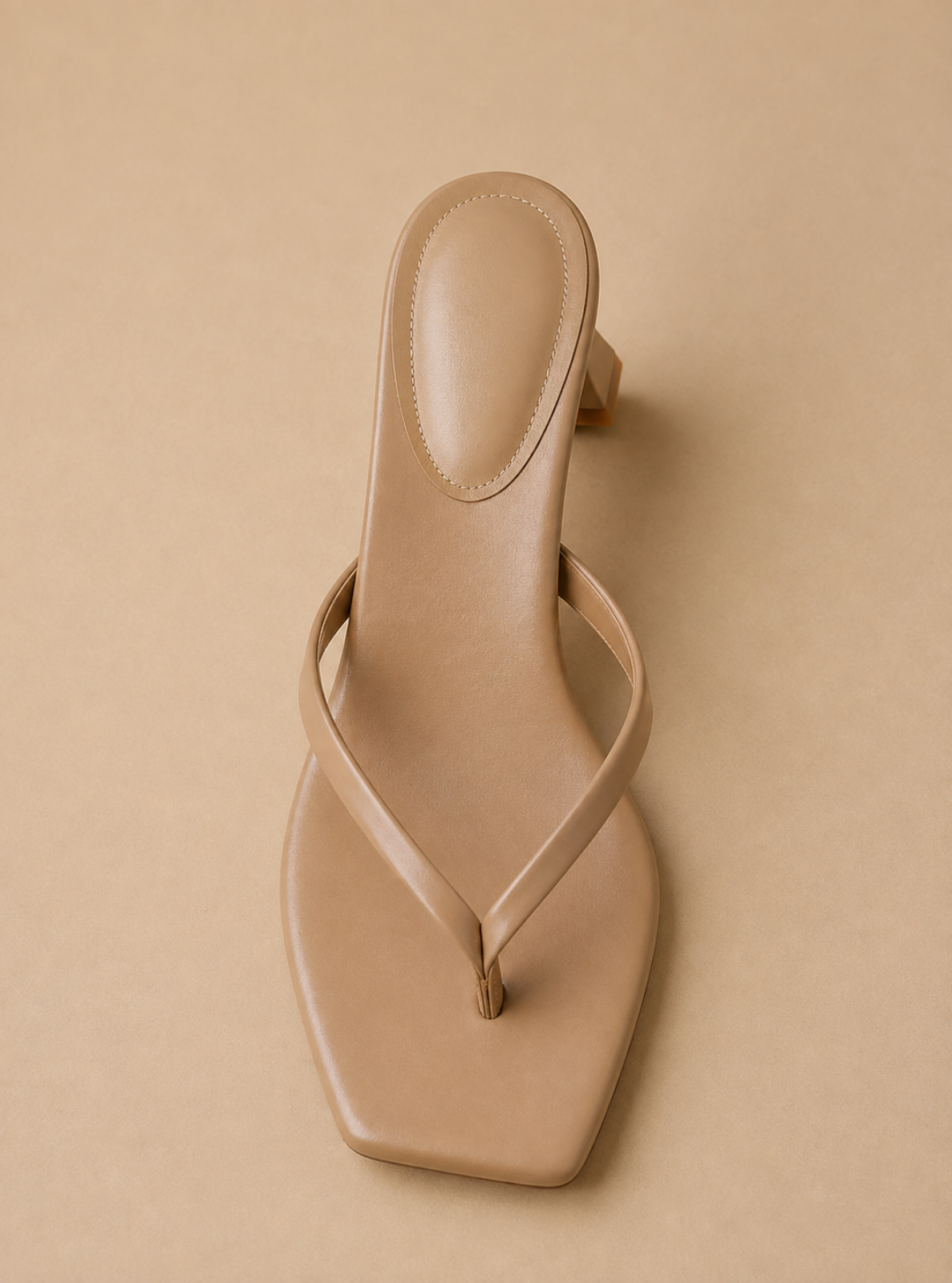 A single beige leather thong sandal with a square toe and a low block heel, photographed from a top-down angle on a matching beige background.