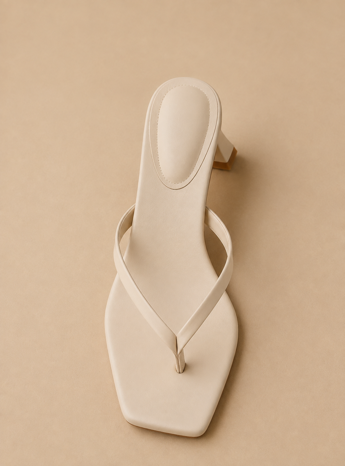 A single cream-colored faux leather thong sandal with a square toe and a low block heel, shown from a top-down view on a solid beige background.